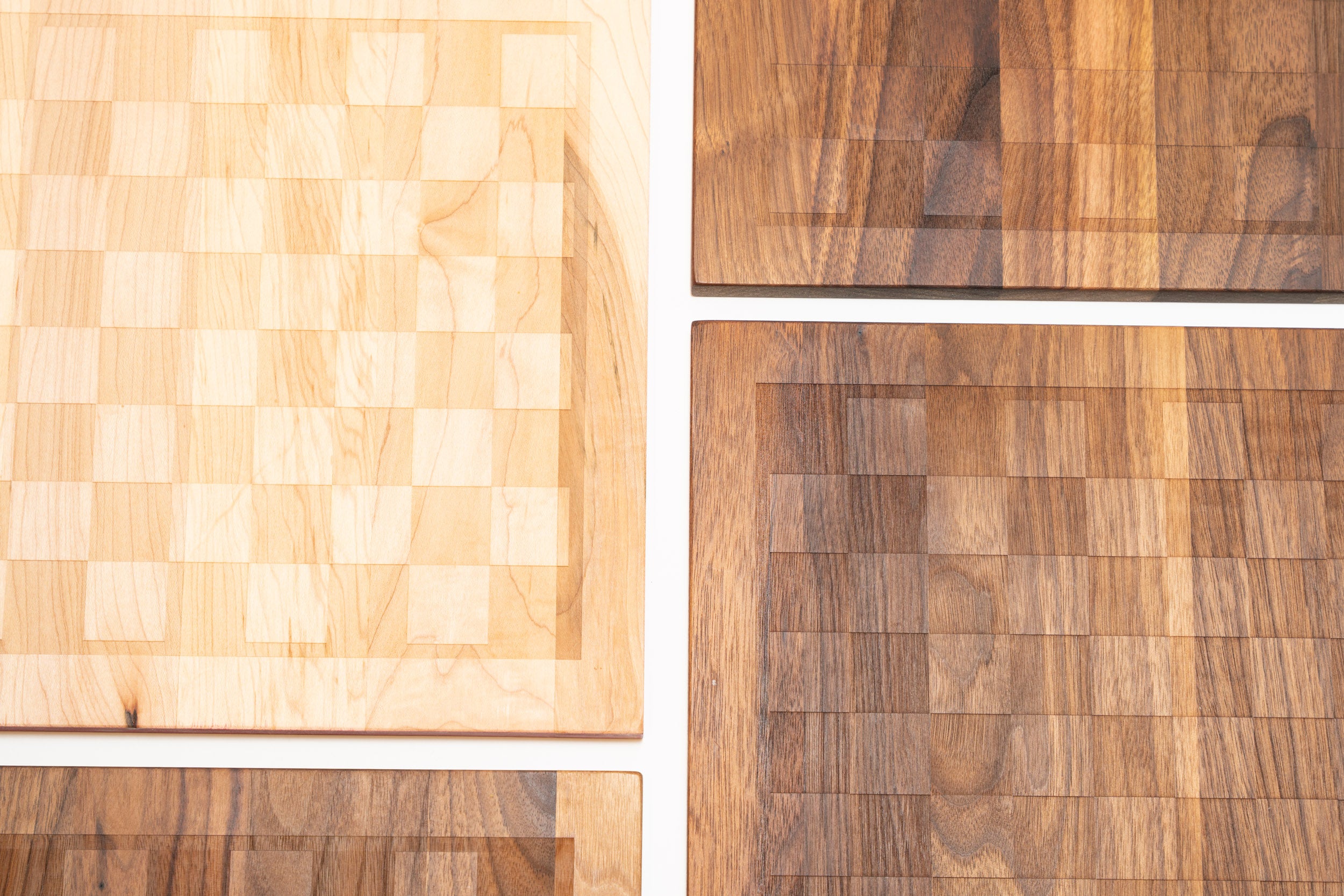Four Snackgammon boards on a white background, one in maple and three in walnut, each showing the etched eight-by-eight game grid.