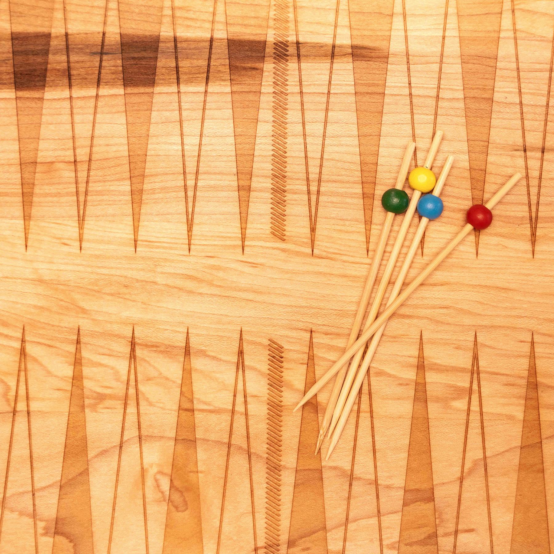 Close-up of the laser-etched backgammon points on a North American maple Snackgammon board, four colored wooden ball picks resting across them.