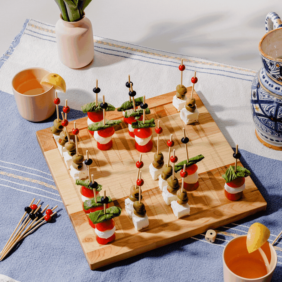Two hands playing on a North American maple Snackgammon board, moving a cube of feta across the etched points.