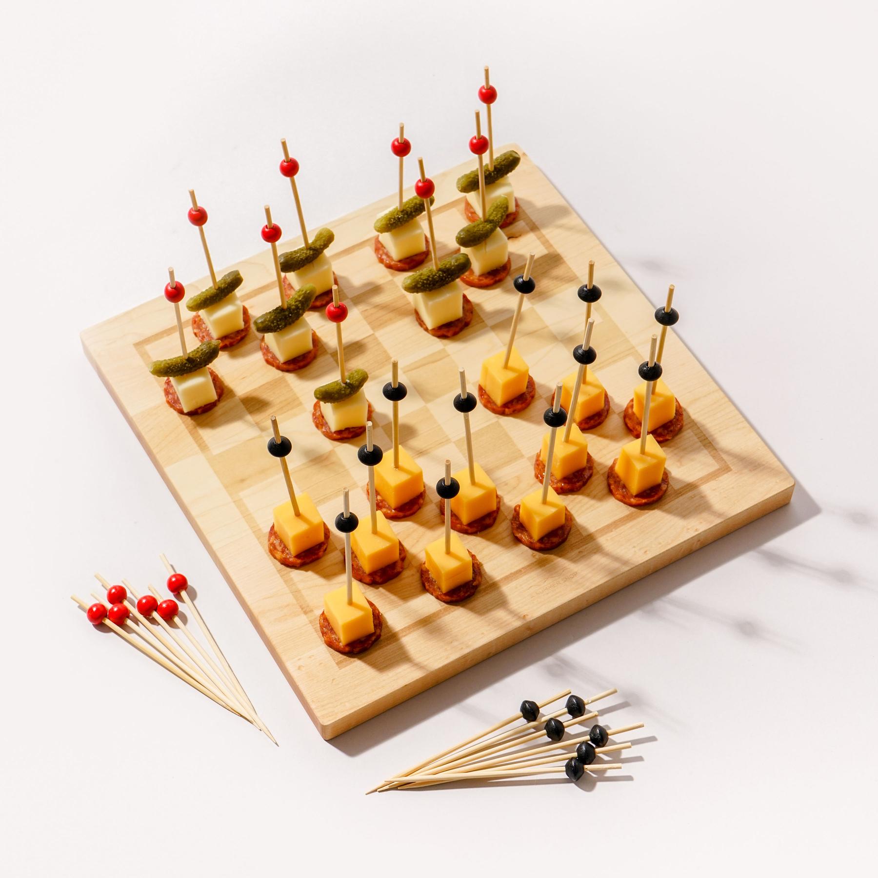 A maple Snackgammon board set up as a checkers game, with cubes of cheese and slices of salami on cocktail picks standing in for the playing pieces.