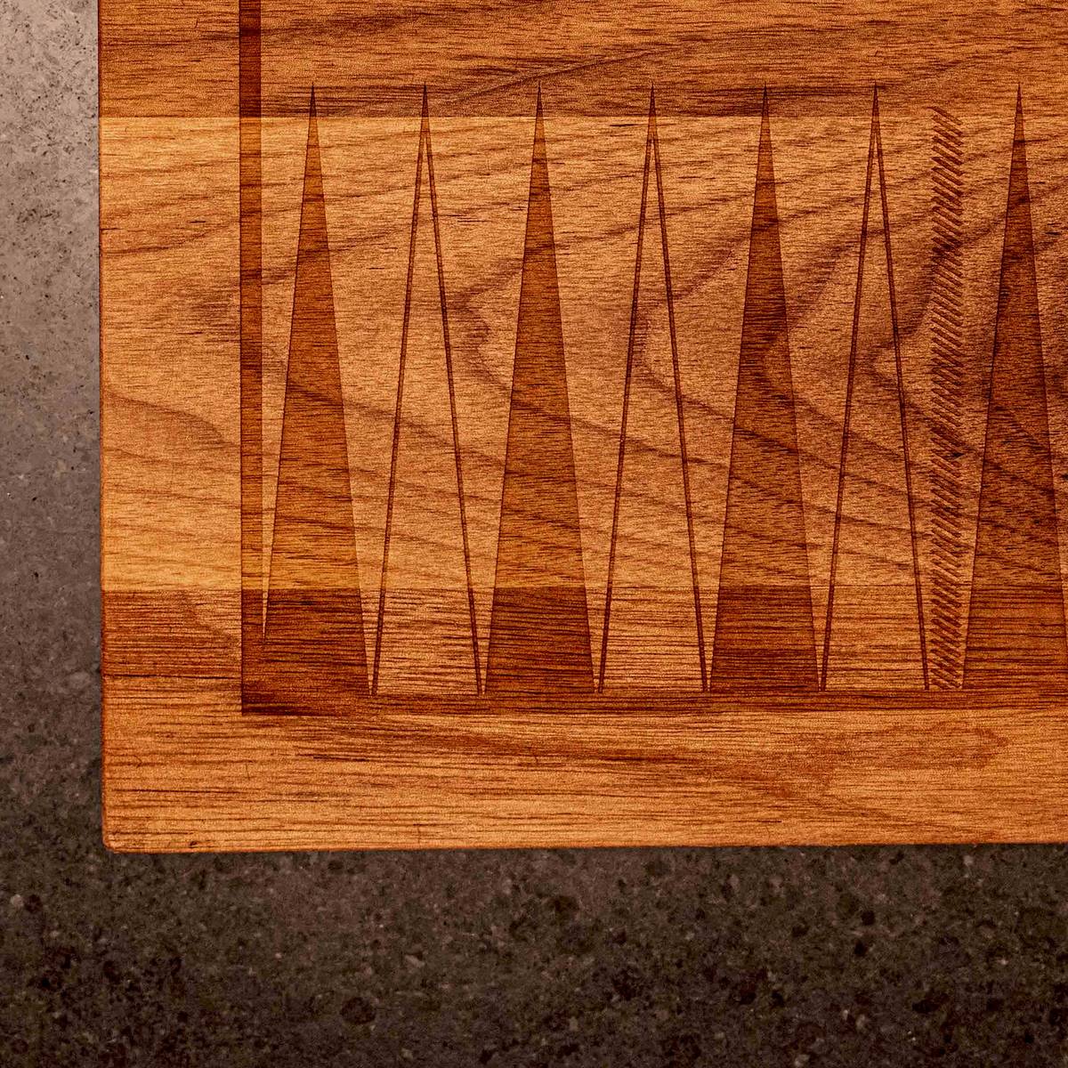 Close-up of the laser-etched backgammon points on the corner of a Snackgammon board resting on a stone counter.